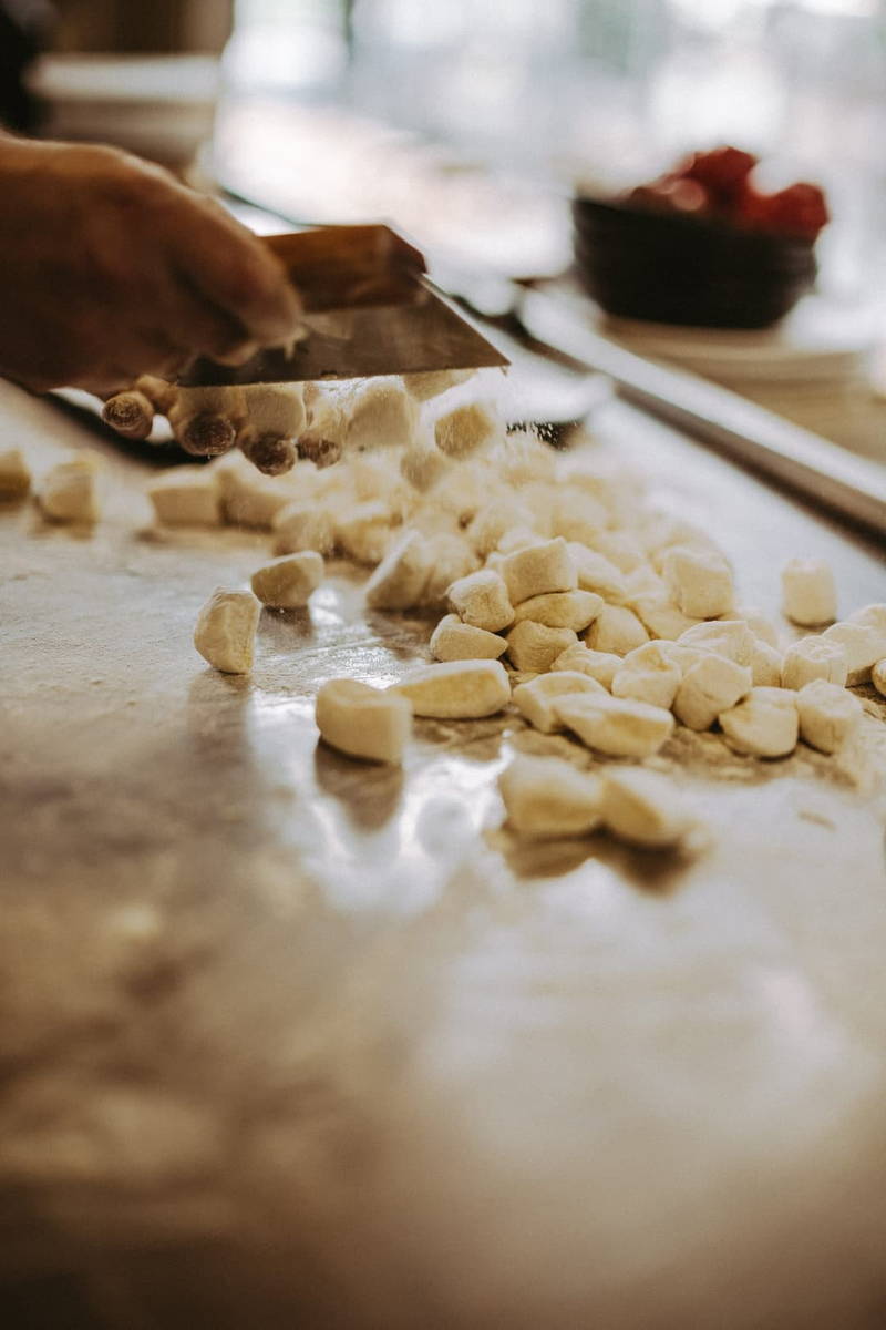 Hands rolling gnocchi on a kitchen bench.
