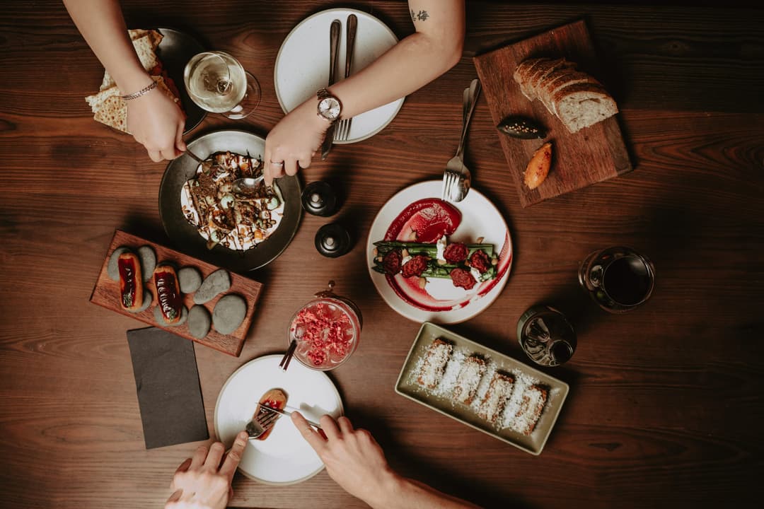 A shared table mid service, plates and hands.